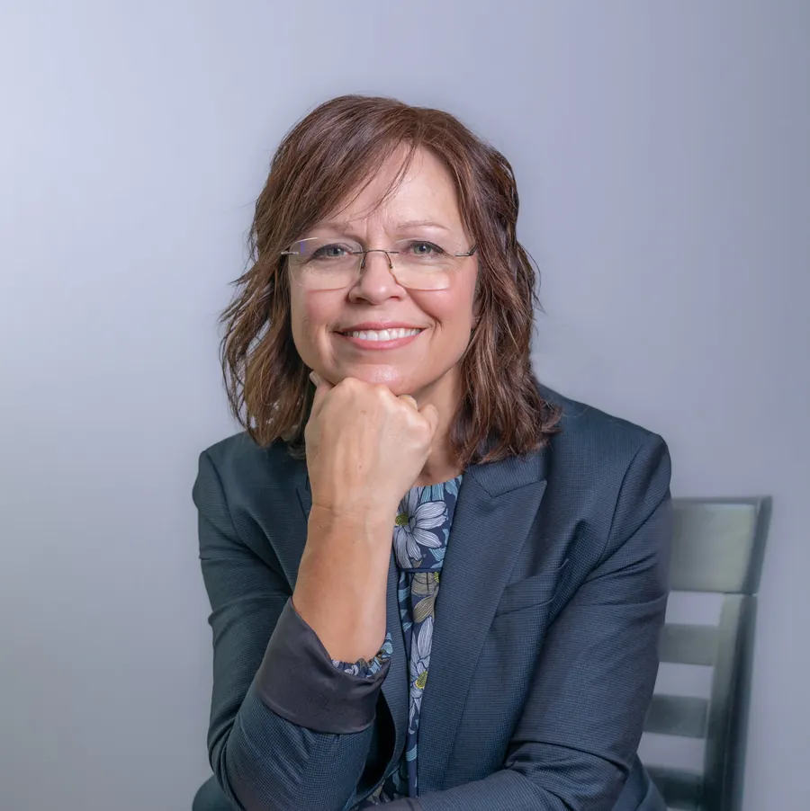 Portrait of Jody Powers smiling, wearing glasses and a navy blazer